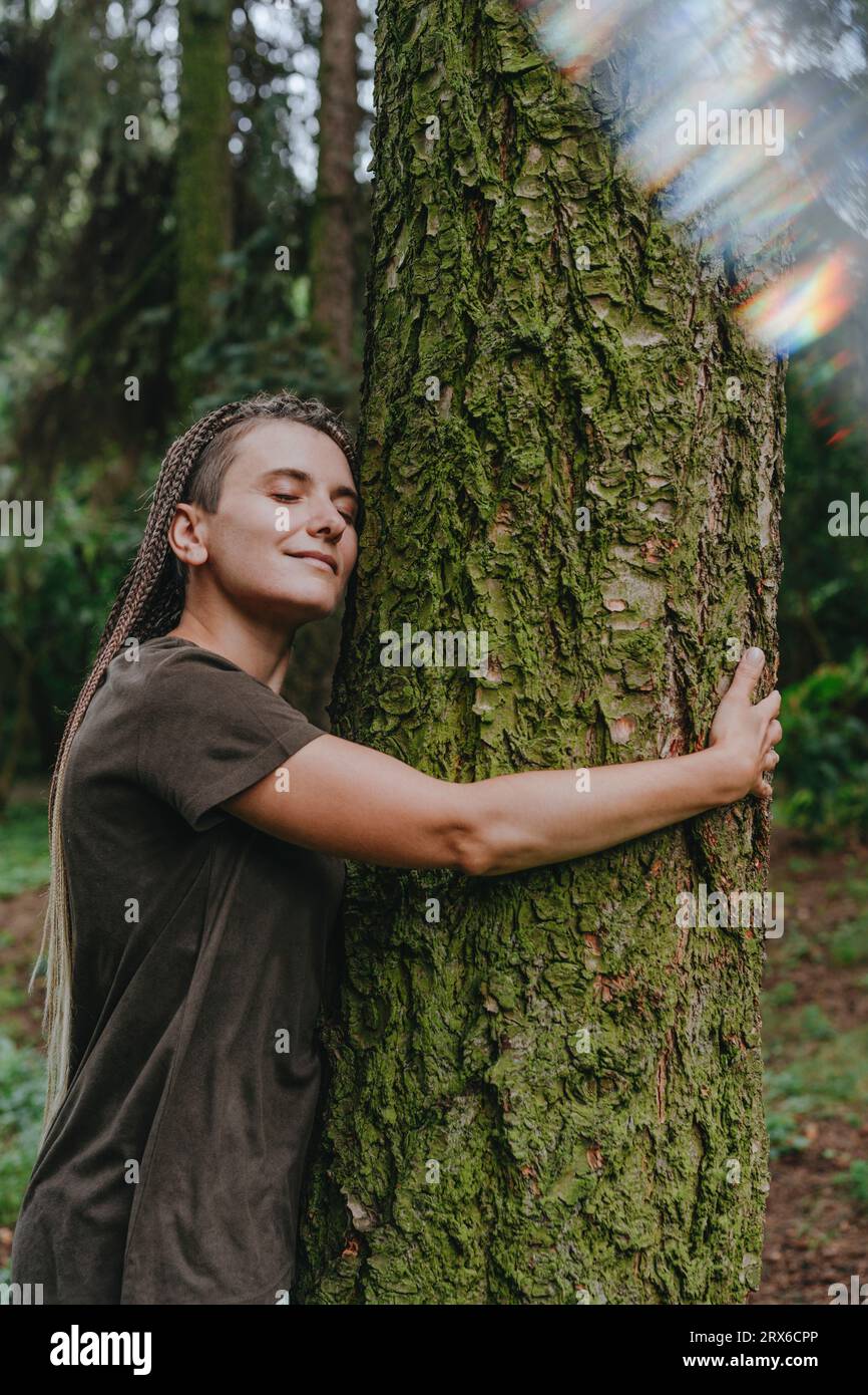 Donna abbracciando albero nella foresta Foto Stock