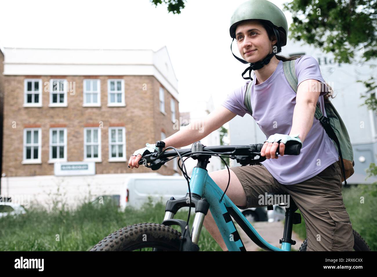 Donna sorridente che indossa il casco seduta in bicicletta Foto Stock