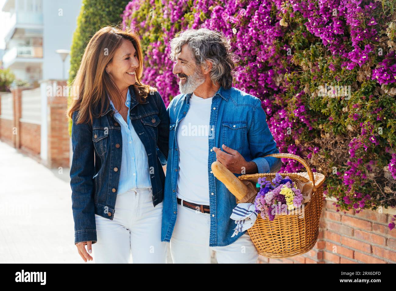 Felice coppia anziana con cestino da picnic vicino al muro dei fiori Foto Stock