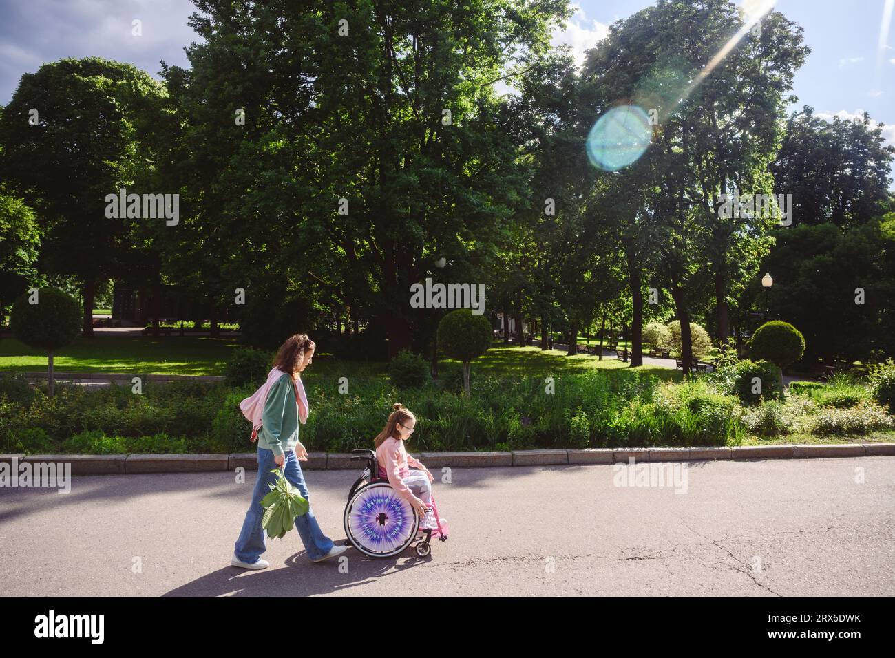 Figlia in sedia a rotelle con mamma che cammina al parco in estate Foto Stock