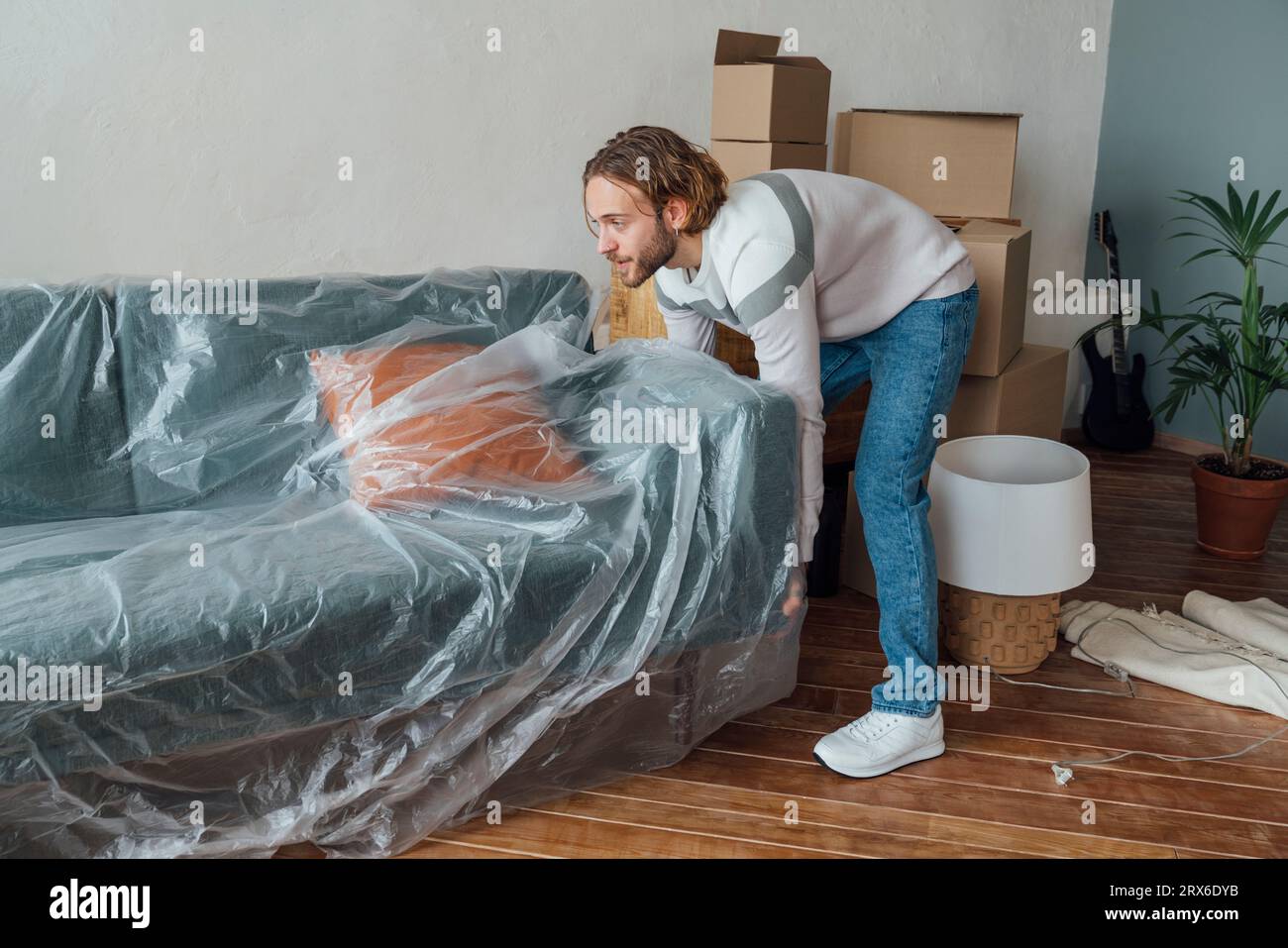 Giovane uomo che copre il divano con la plastica a casa Foto Stock