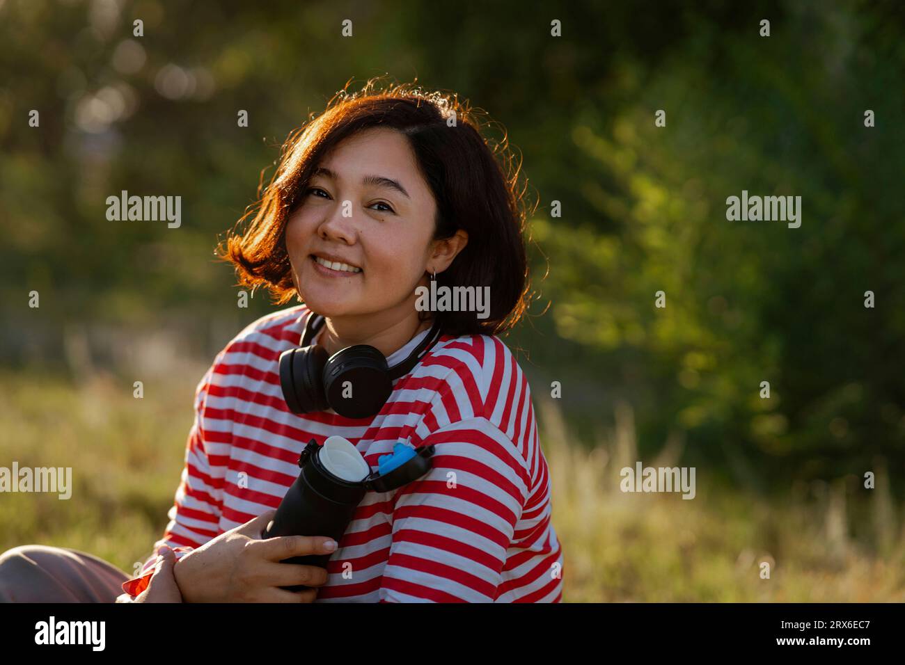 Donna sorridente con bottiglia d'acqua e cuffie sul campo Foto Stock