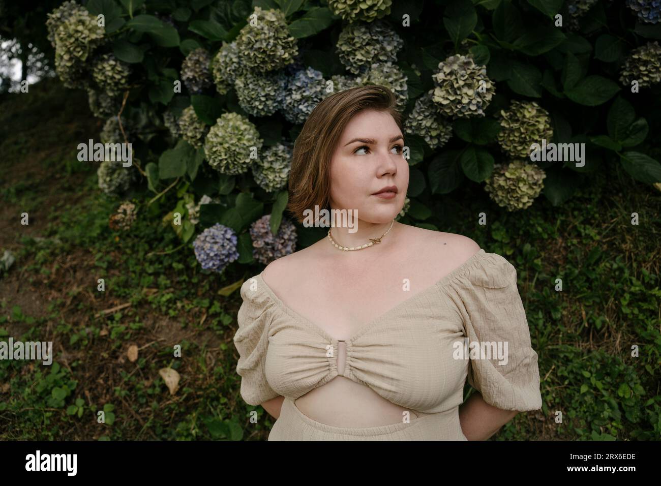 Donna contemplativa in piedi di fronte a piante di fiori di ortensia Foto Stock