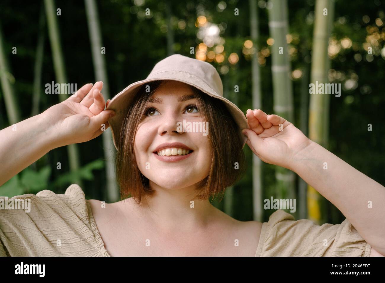 Donna contemplativa che indossa un cappello a secchiello vicino alle piante di bambù Foto Stock