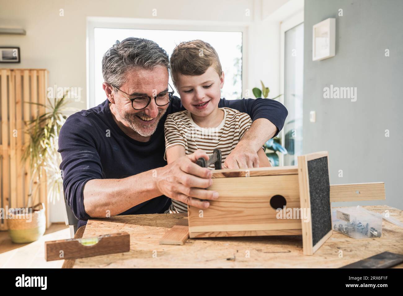 Un uomo e un ragazzo sorridenti che costruiscono una casa per uccelli in legno a casa Foto Stock