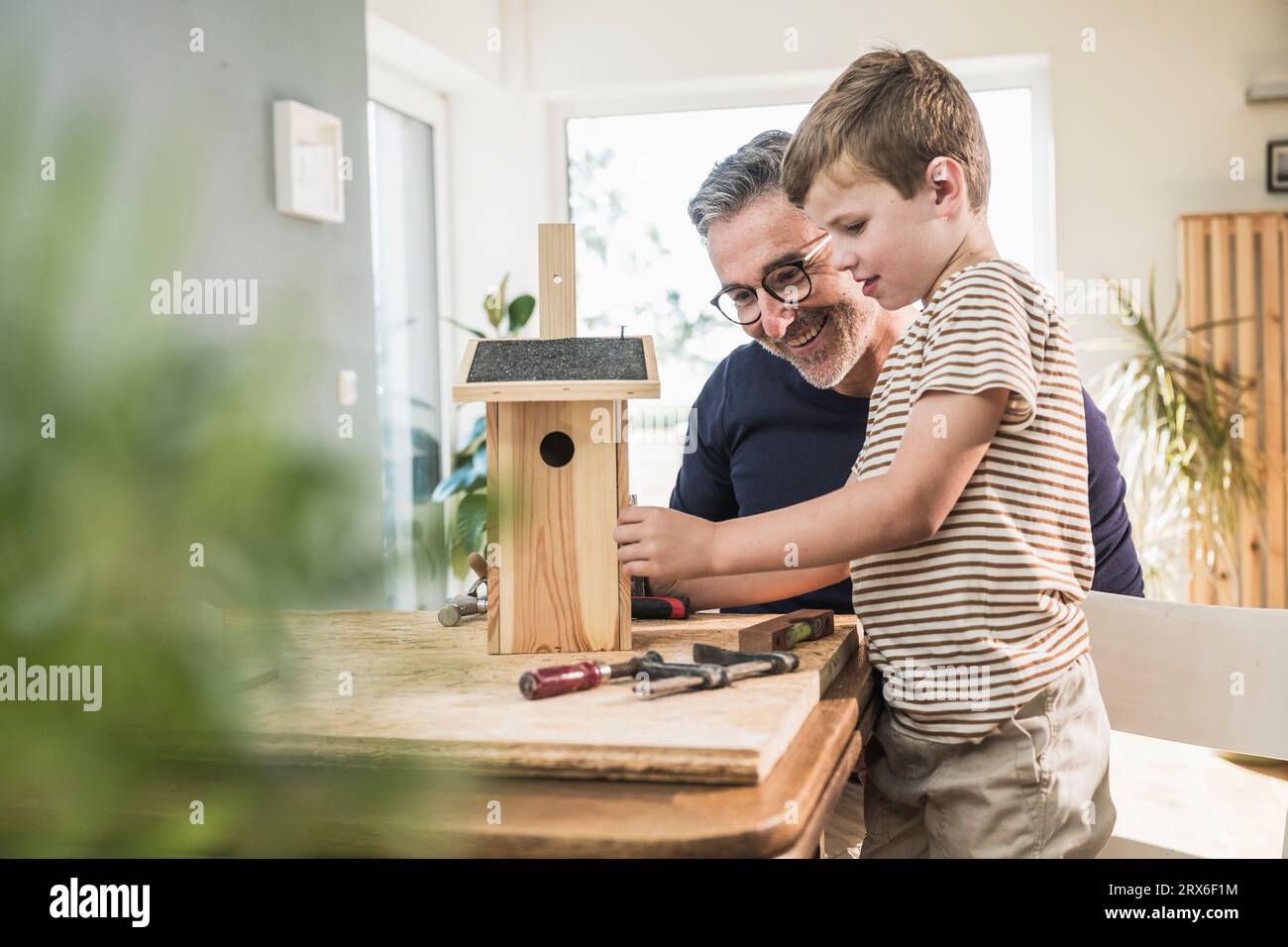 Un uomo sorridente che fa birdhouse in legno con nipote a casa Foto Stock