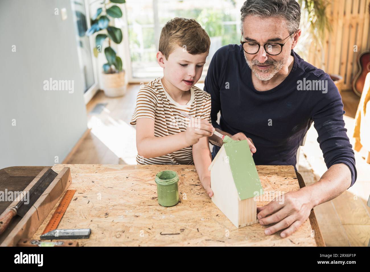 Nipote che dipinge la casa modello dal nonno sul tavolo Foto Stock