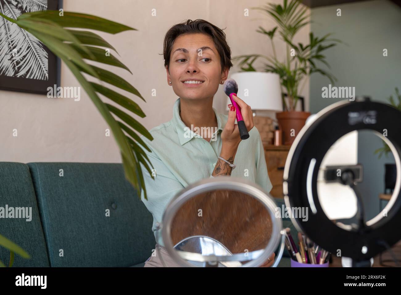 Influencer sorridente che fa make-up e vlogging tramite smartphone a casa Foto Stock