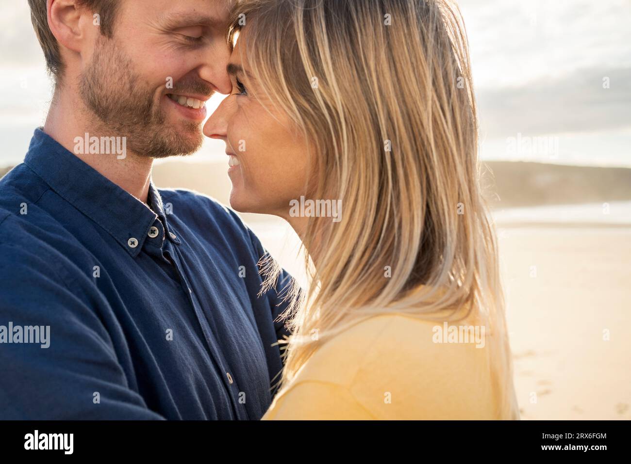 Uomo sorridente che abbraccia la donna in spiaggia Foto Stock