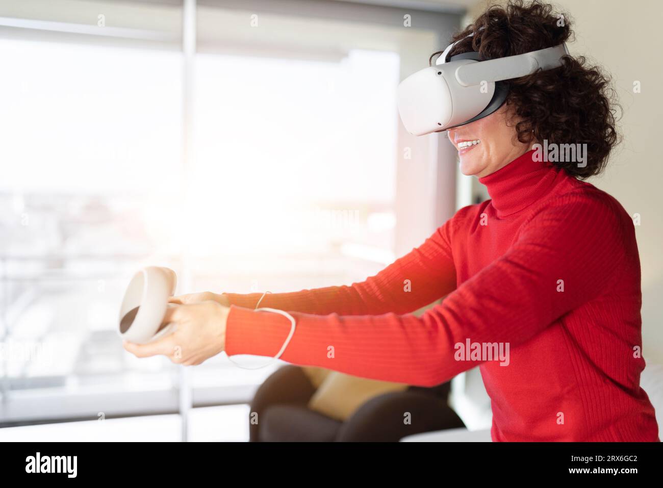 Donna sorridente che indossa un visore per la realtà virtuale che gioca a casa Foto Stock