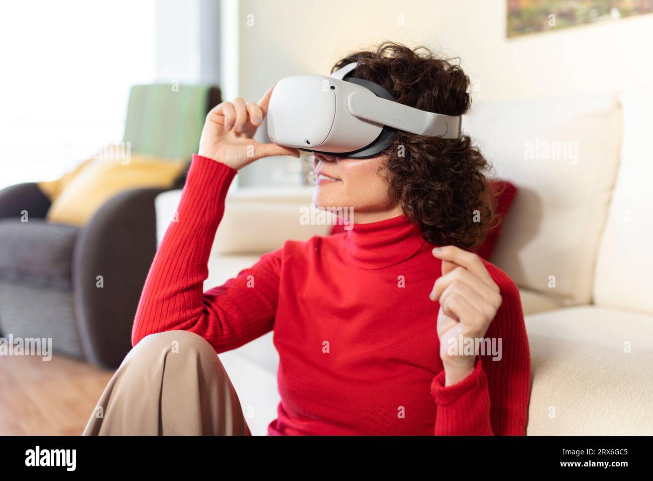 Donna sorridente che indossa un visore per la realtà virtuale seduta a casa Foto Stock