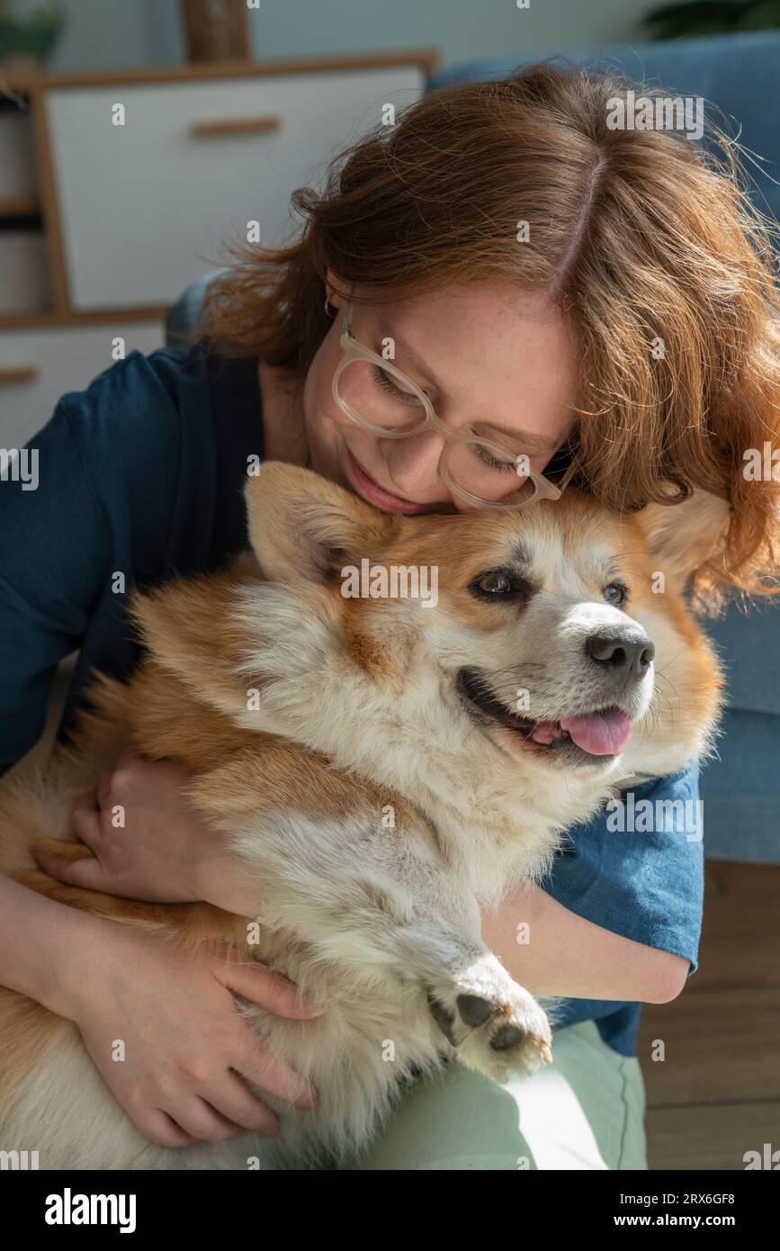 Donna che abbraccia il cane Corgi gallese a casa Foto Stock