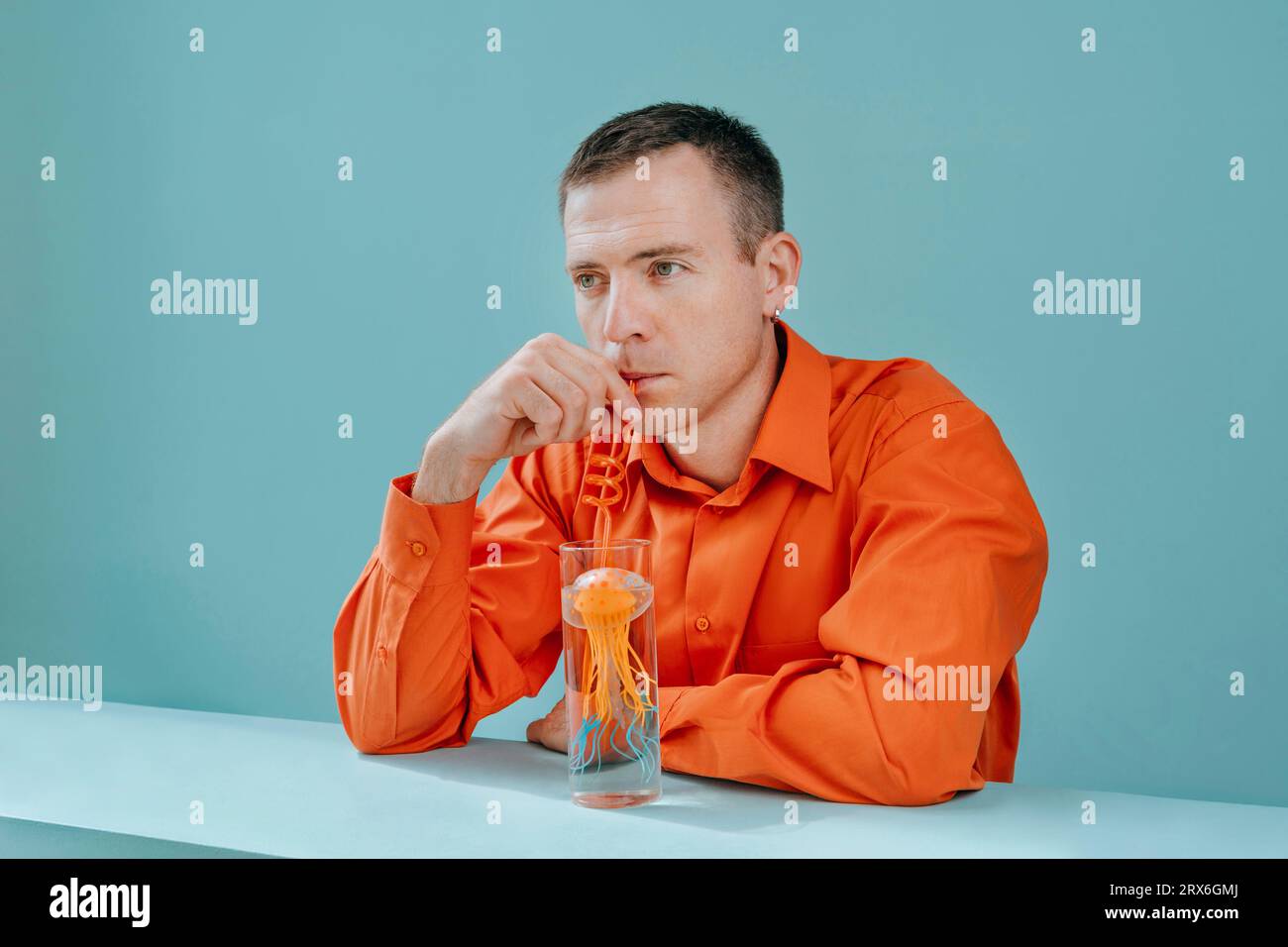 Uomo che beve acqua usando cannuccia di vetro con meduse in studio Foto Stock