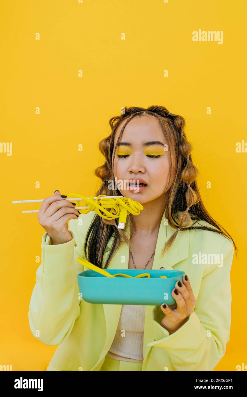 Giovane donna che mangia noodles come filo di bento box su sfondo giallo Foto Stock
