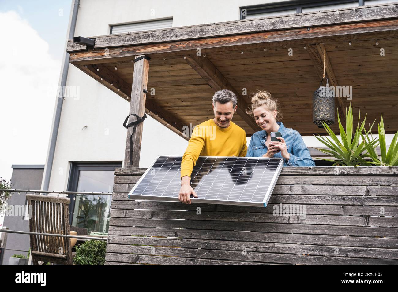 Coppia che installa il pannello solare su un balcone di legno Foto Stock