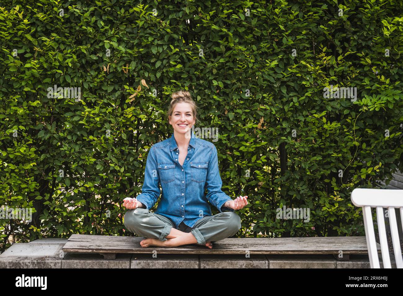Ritratto di una donna che meditava sulla panchina di fronte alla siepe Foto Stock