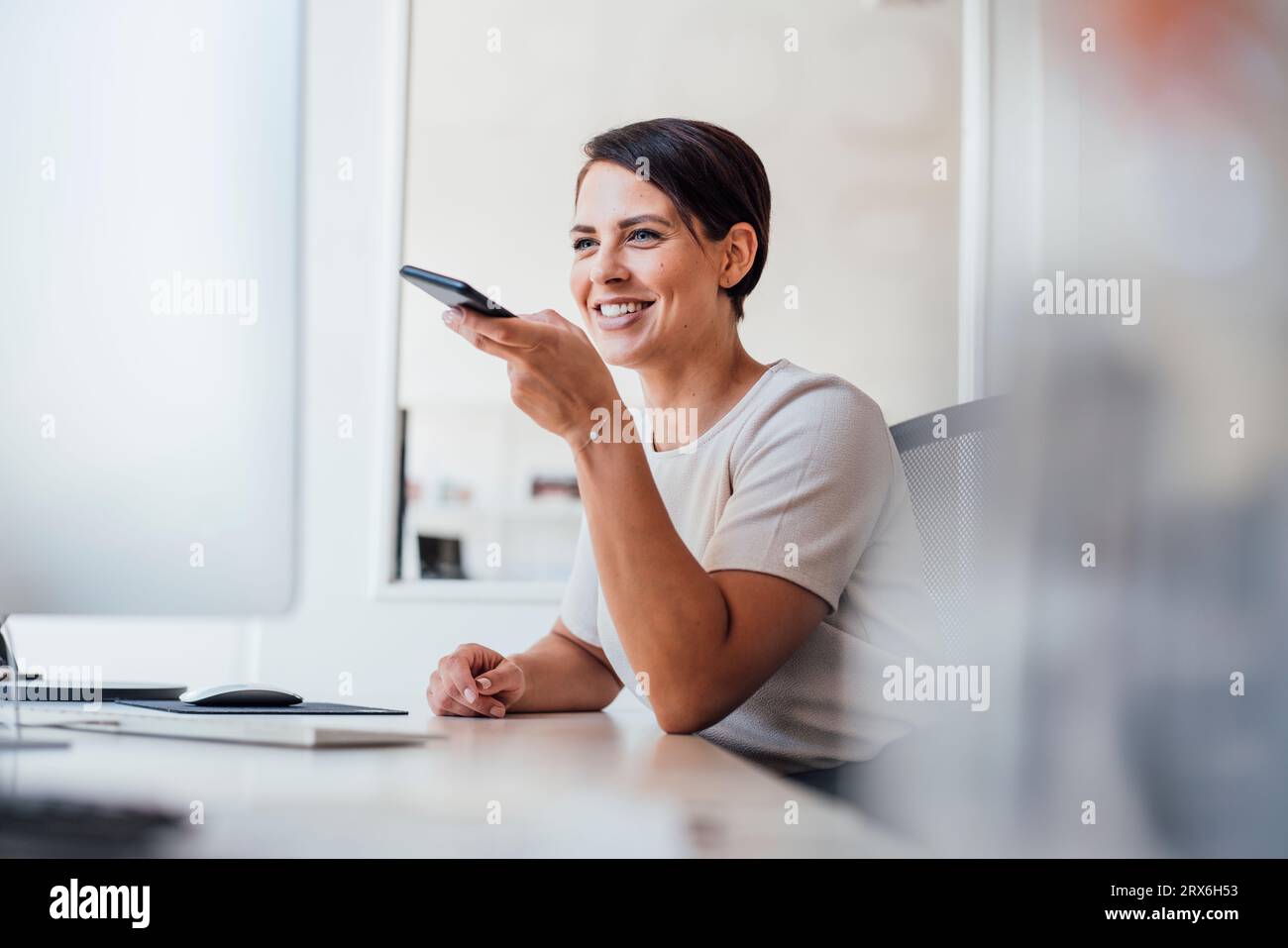 Donna d'affari felice che invia messaggi vocali sullo smartphone Foto Stock