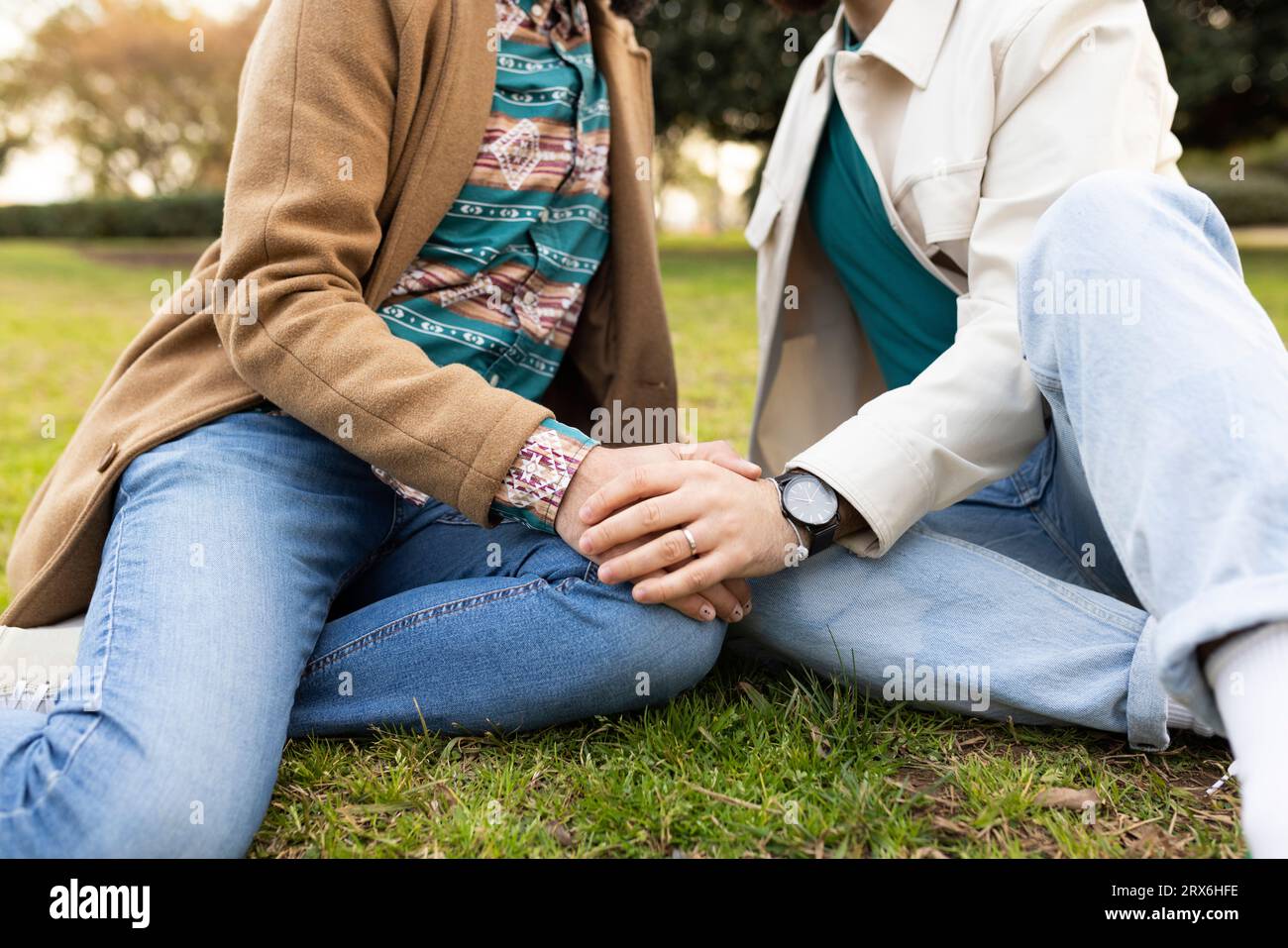 Coppia gay che si tiene per mano e si siede insieme sull'erba Foto Stock