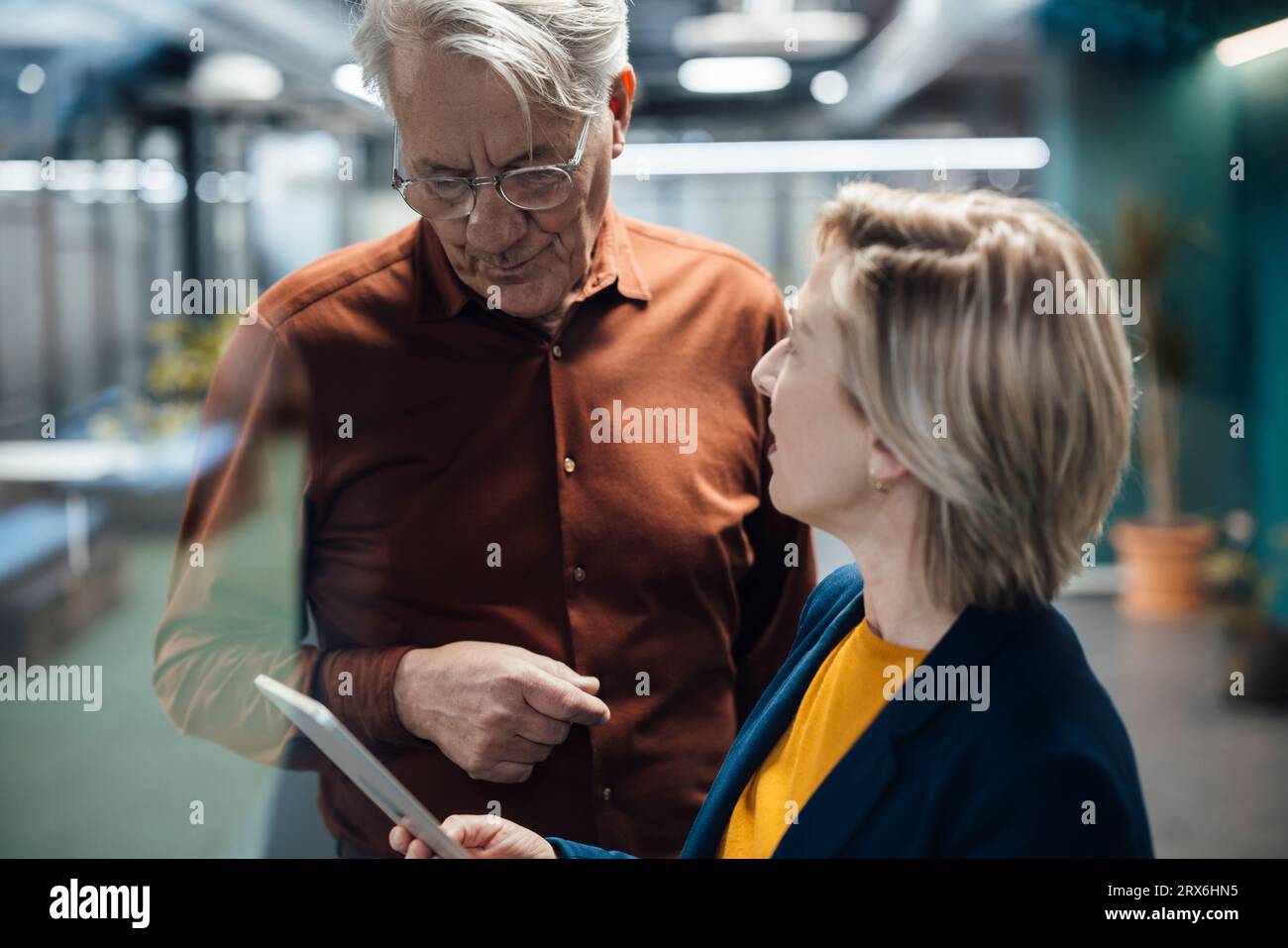 Donna d'affari in possesso di un tablet PC che parla con un collega sul posto di lavoro Foto Stock