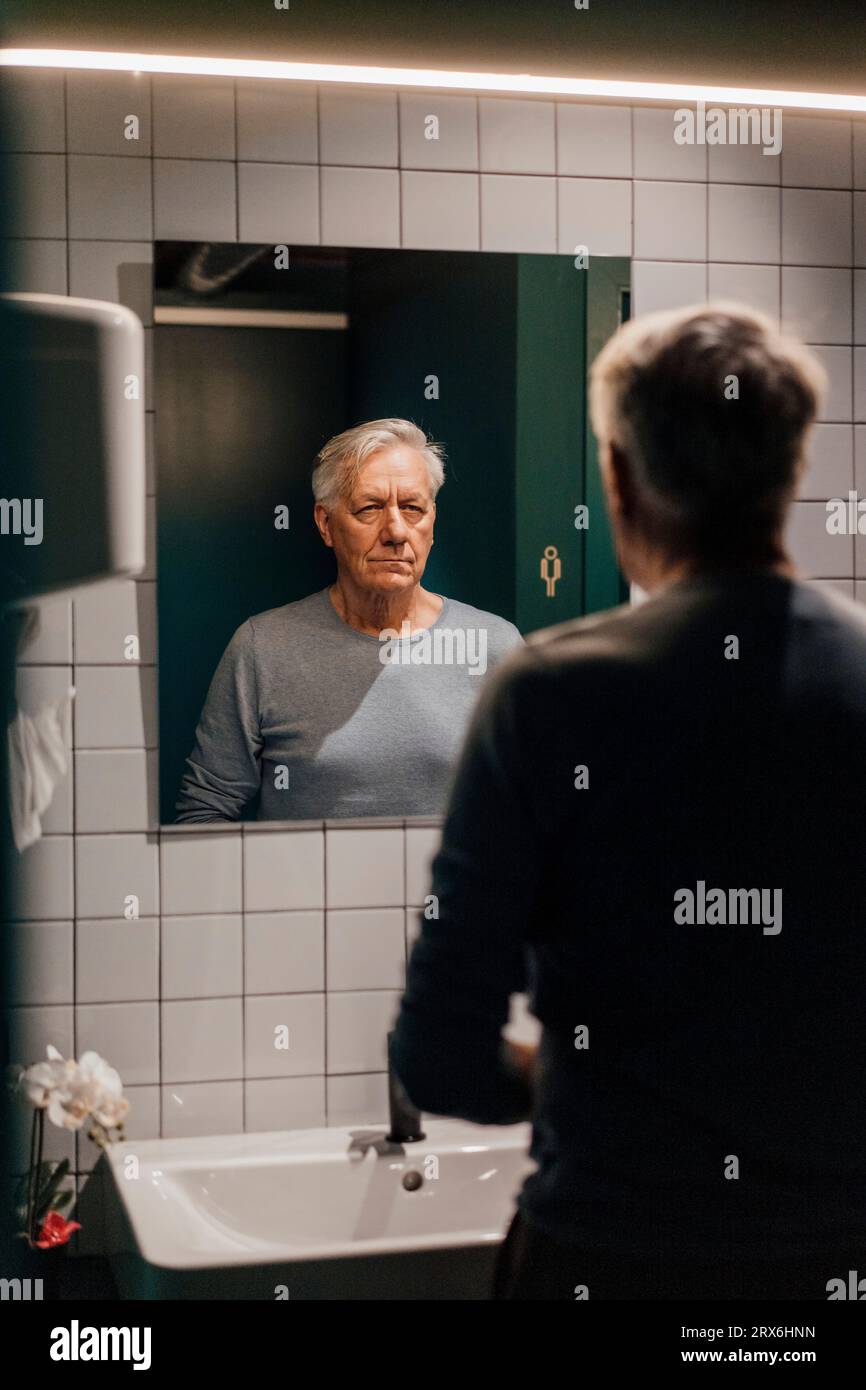 Senior uomo cercando in specchio nella sala da bagno Foto Stock