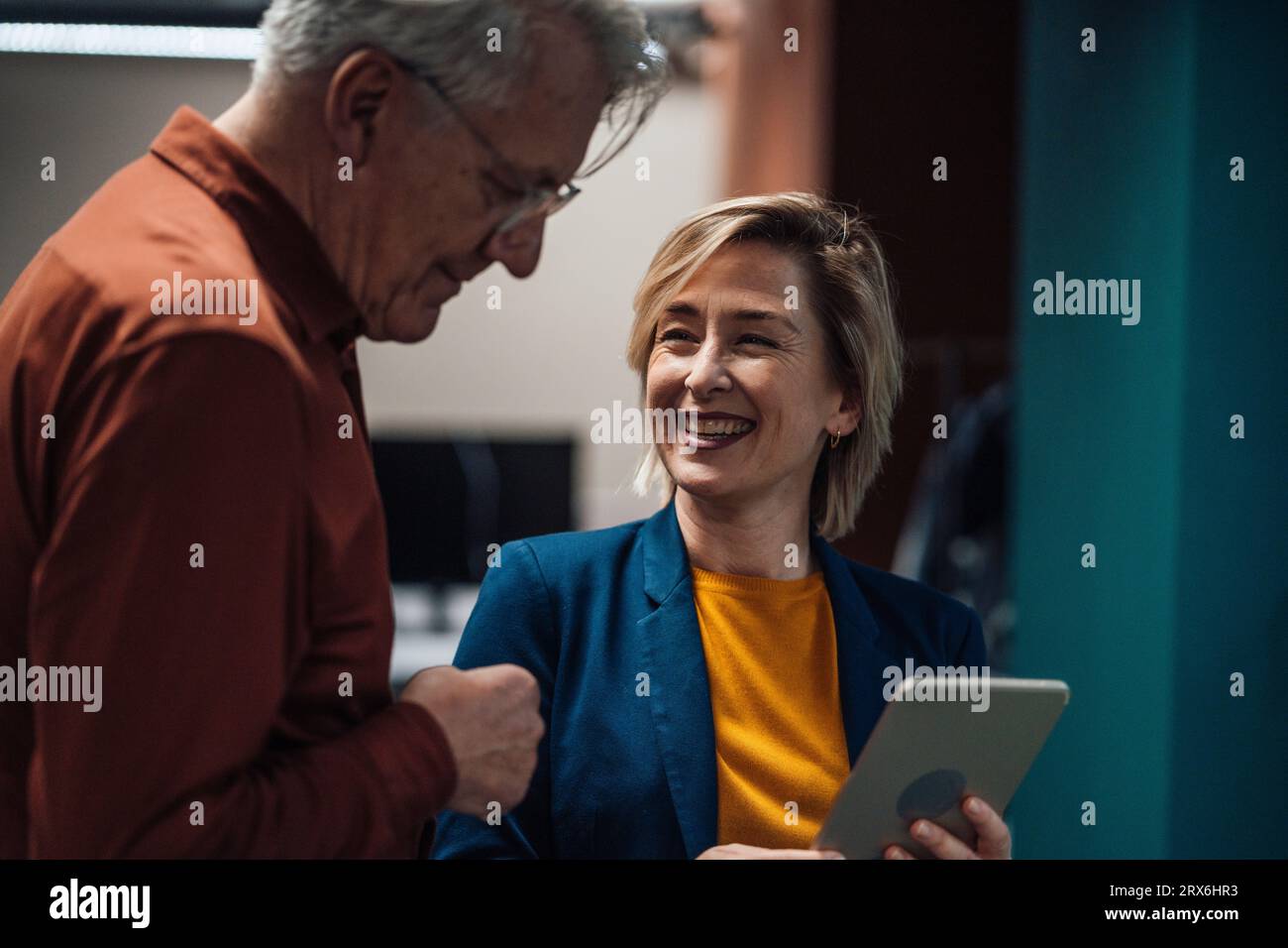 Donna d'affari felice con un tablet che parla con un collega sul posto di lavoro Foto Stock