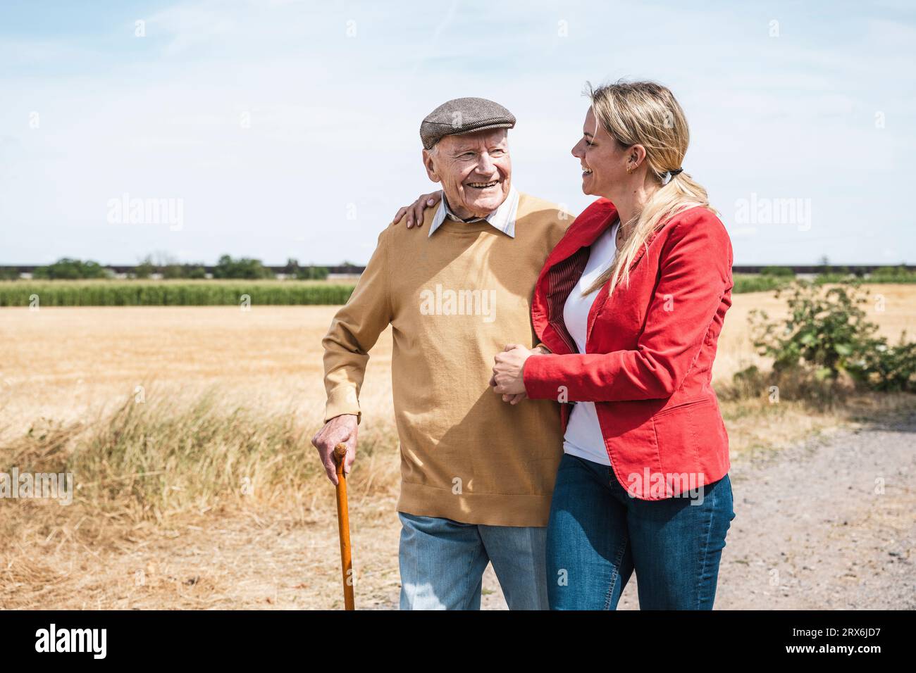 Un uomo anziano sorridente che cammina con una donna a campo nelle giornate di sole Foto Stock