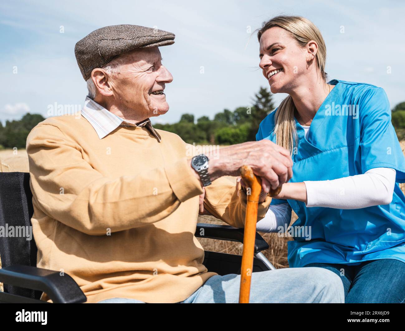 Lavoratore sanitario felice che parla con un uomo anziano seduto in sedia a rotelle Foto Stock