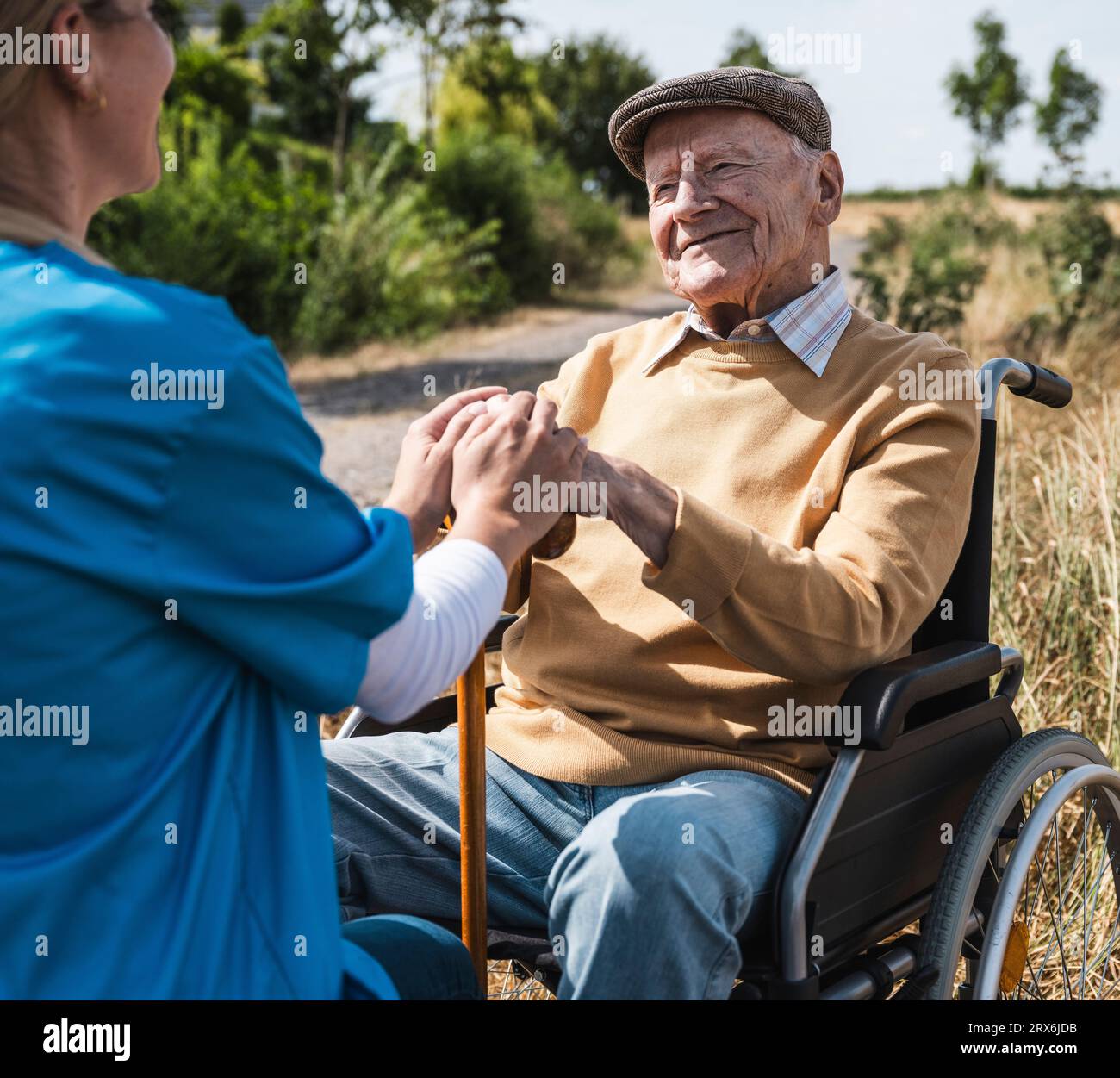 Operatore sanitario che tiene per mano un anziano seduto in sedia a rotelle Foto Stock