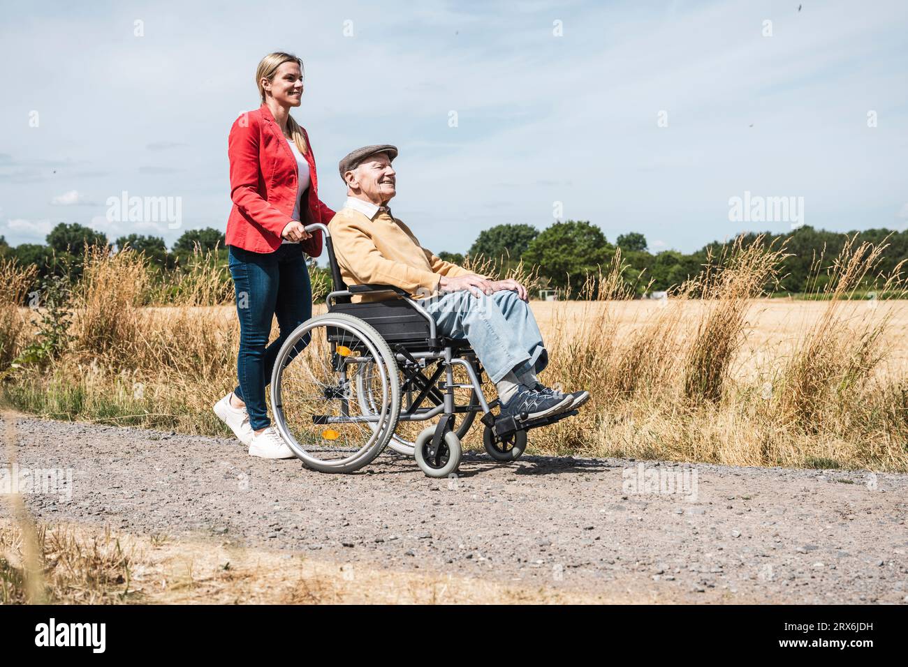 Donna che spinge un uomo anziano seduto in sedia a rotelle per campo Foto Stock