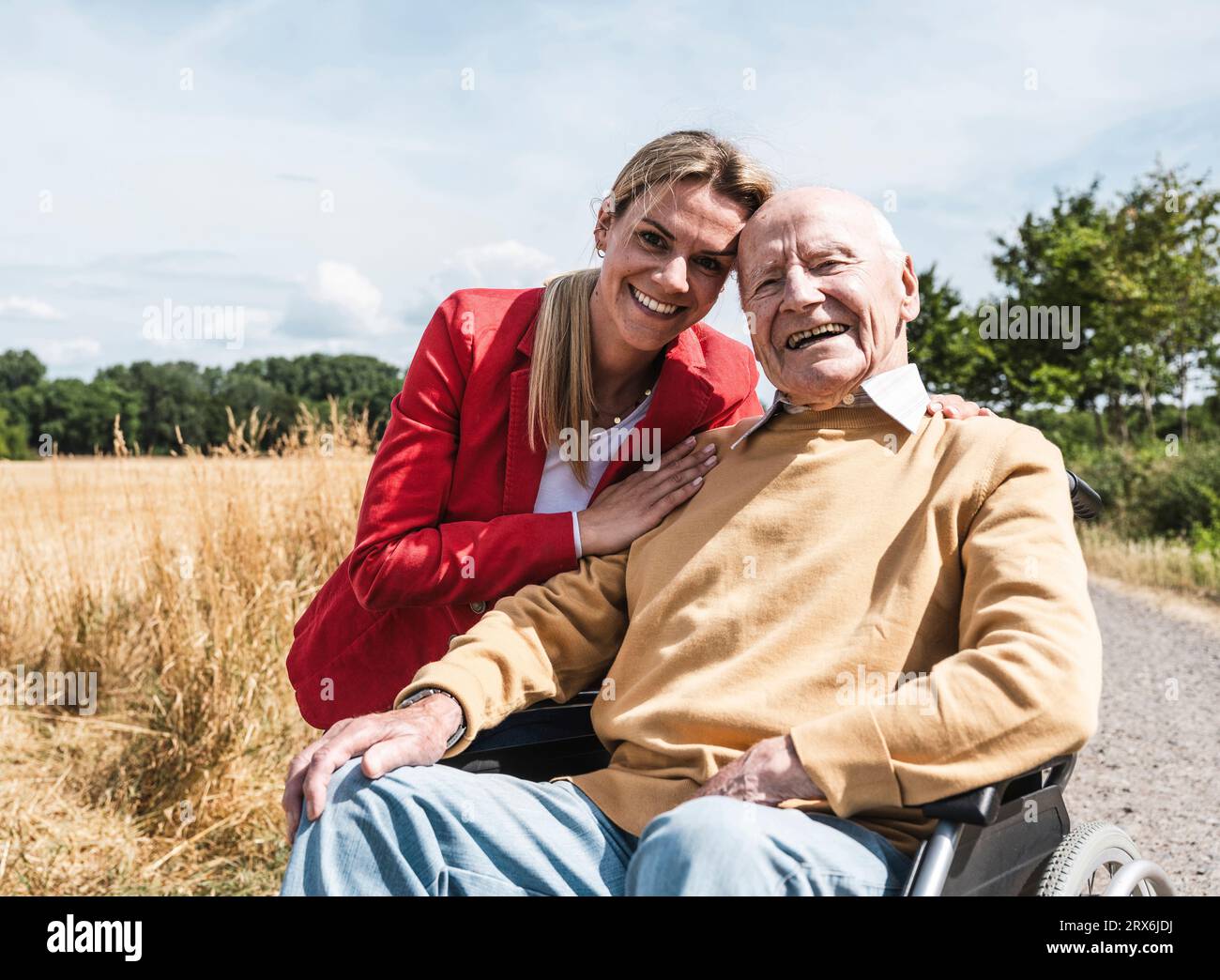 Donna felice con un uomo anziano seduto in sedia a rotelle nelle giornate di sole Foto Stock