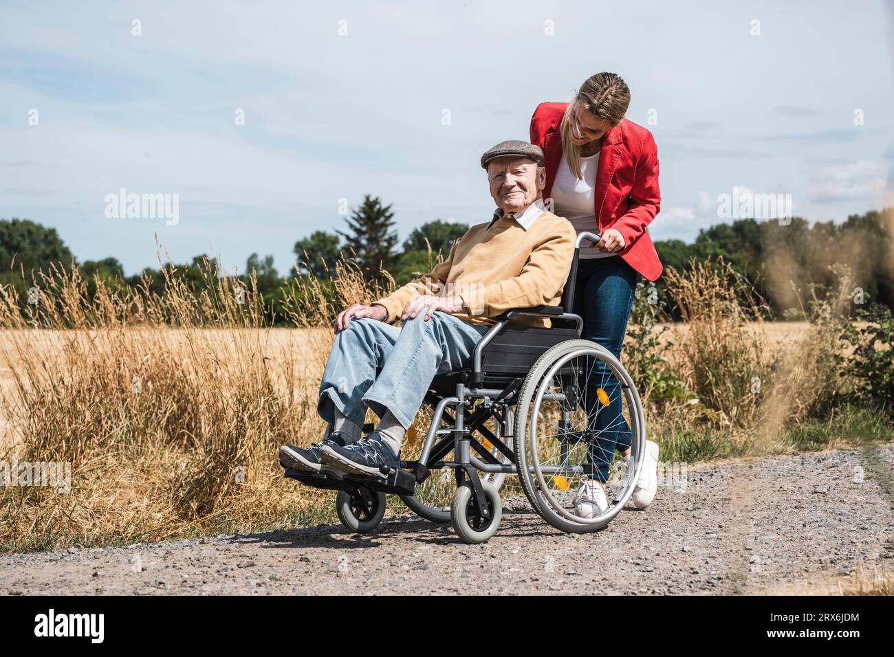 Donna che spinge un uomo anziano con disabilità seduto in sedia a rotelle Foto Stock
