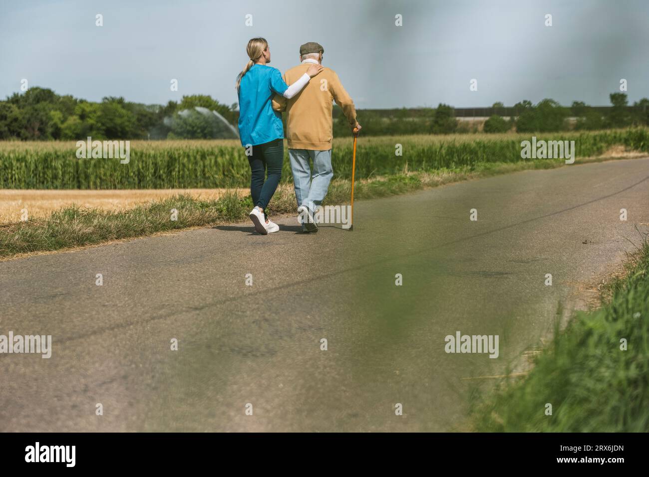 Operatore sanitario che cammina con uomo anziano sulla strada nella giornata di sole Foto Stock