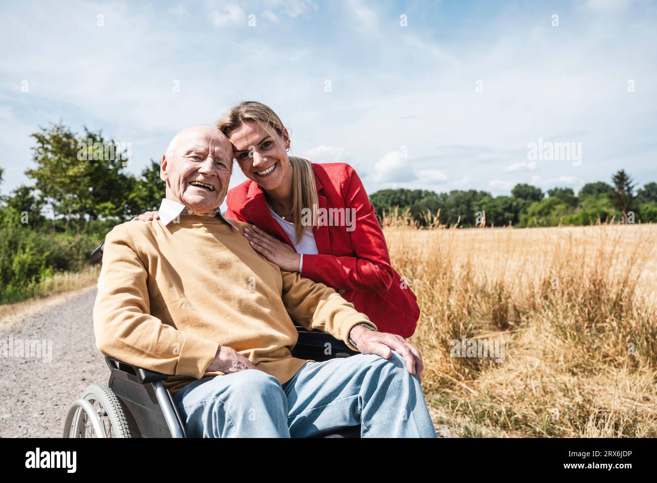 Donna sorridente con un uomo anziano seduto in sedia a rotelle nelle giornate di sole Foto Stock