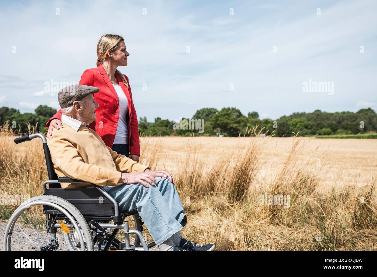 Uomo anziano seduto in sedia a rotelle da una donna e guardando il campo Foto Stock