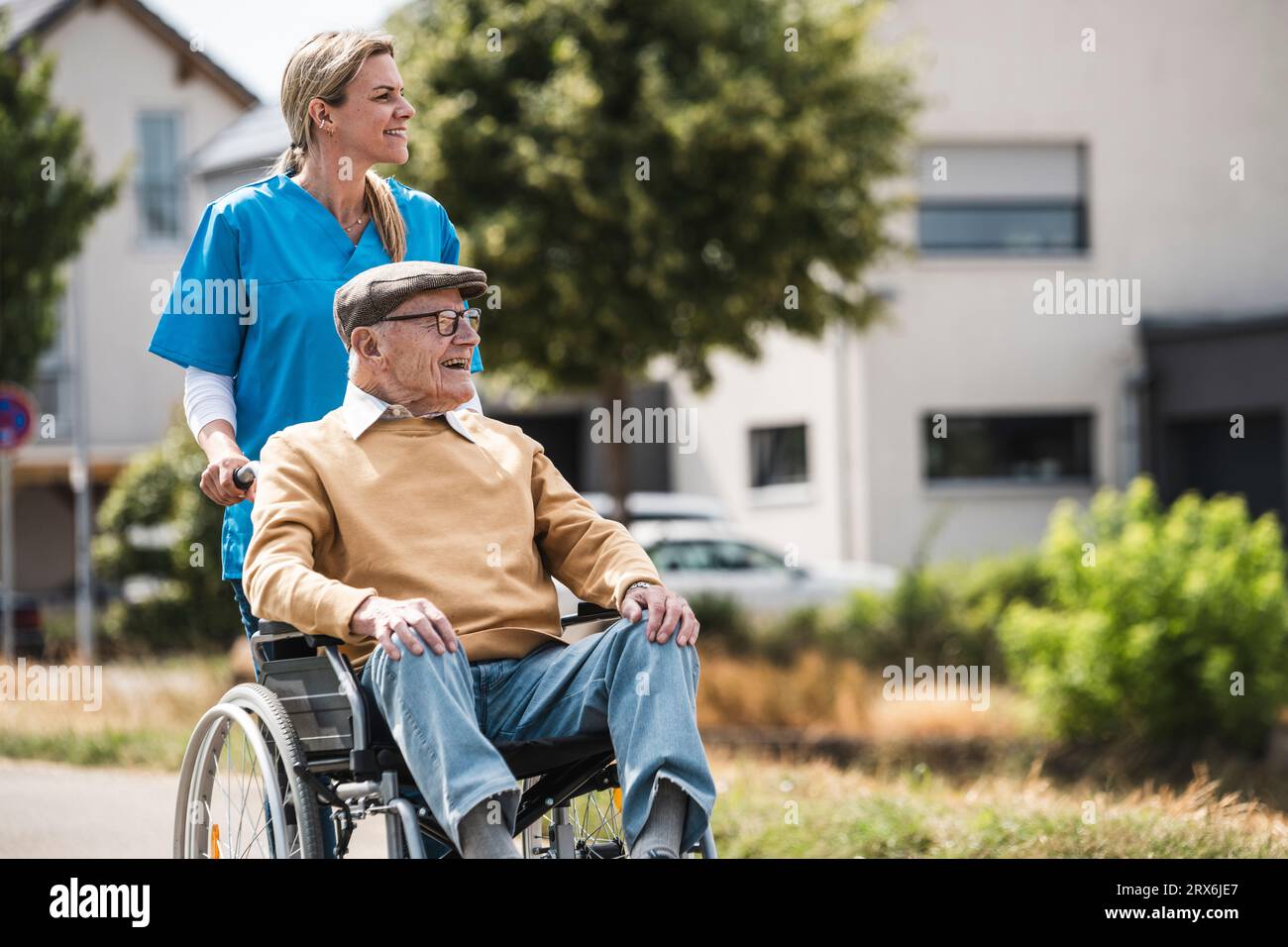 Infermiera sorridente che spinge un uomo anziano seduto in sedia a rotelle Foto Stock