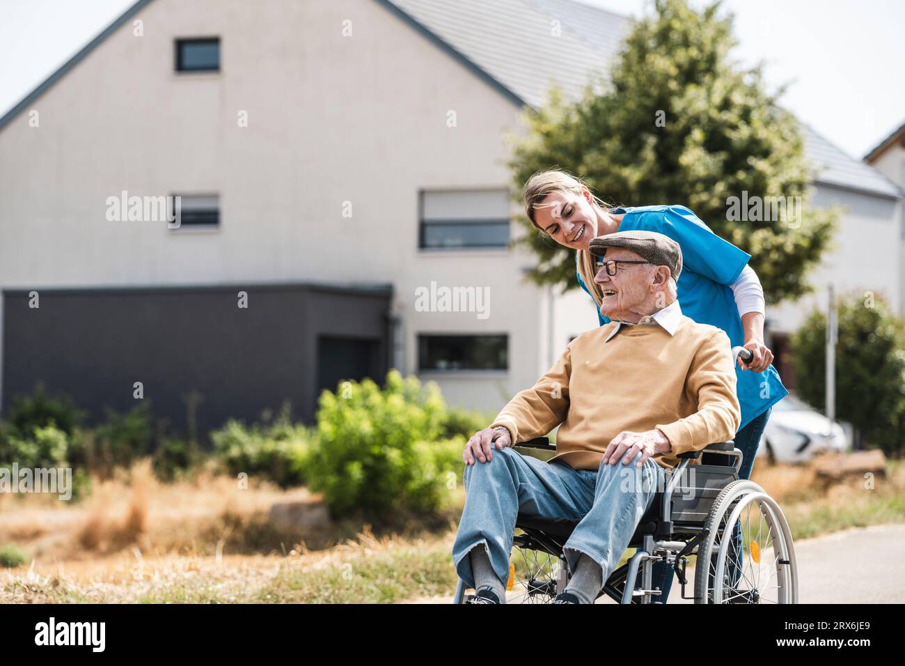 Operatore sanitario che parla e spinge l'uomo anziano seduto in sedia a rotelle Foto Stock