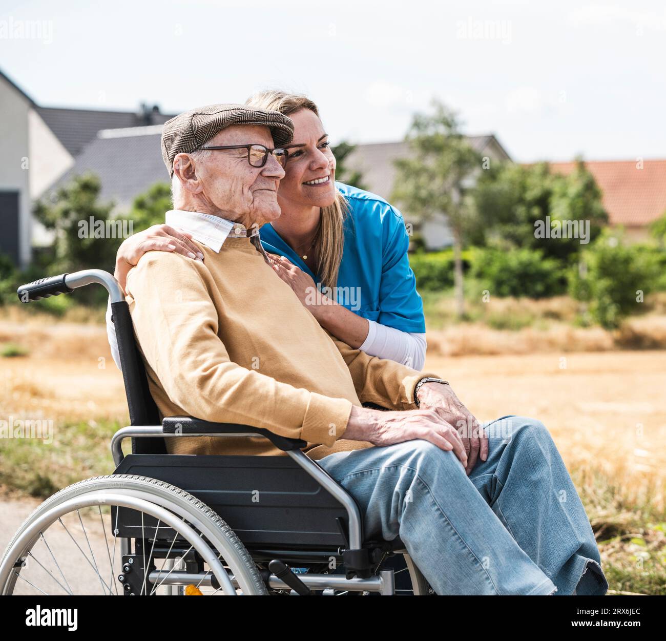 Infermiera sorridente che abbraccia l'uomo anziano seduto in sedia a rotelle Foto Stock