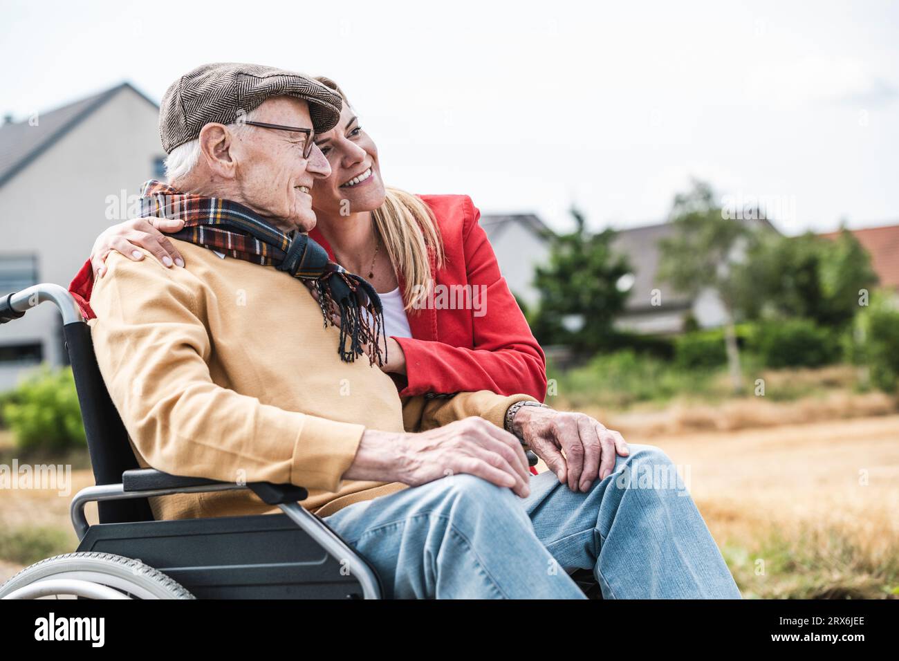 Donna sorridente che abbraccia un uomo anziano seduto in sedia a rotelle Foto Stock