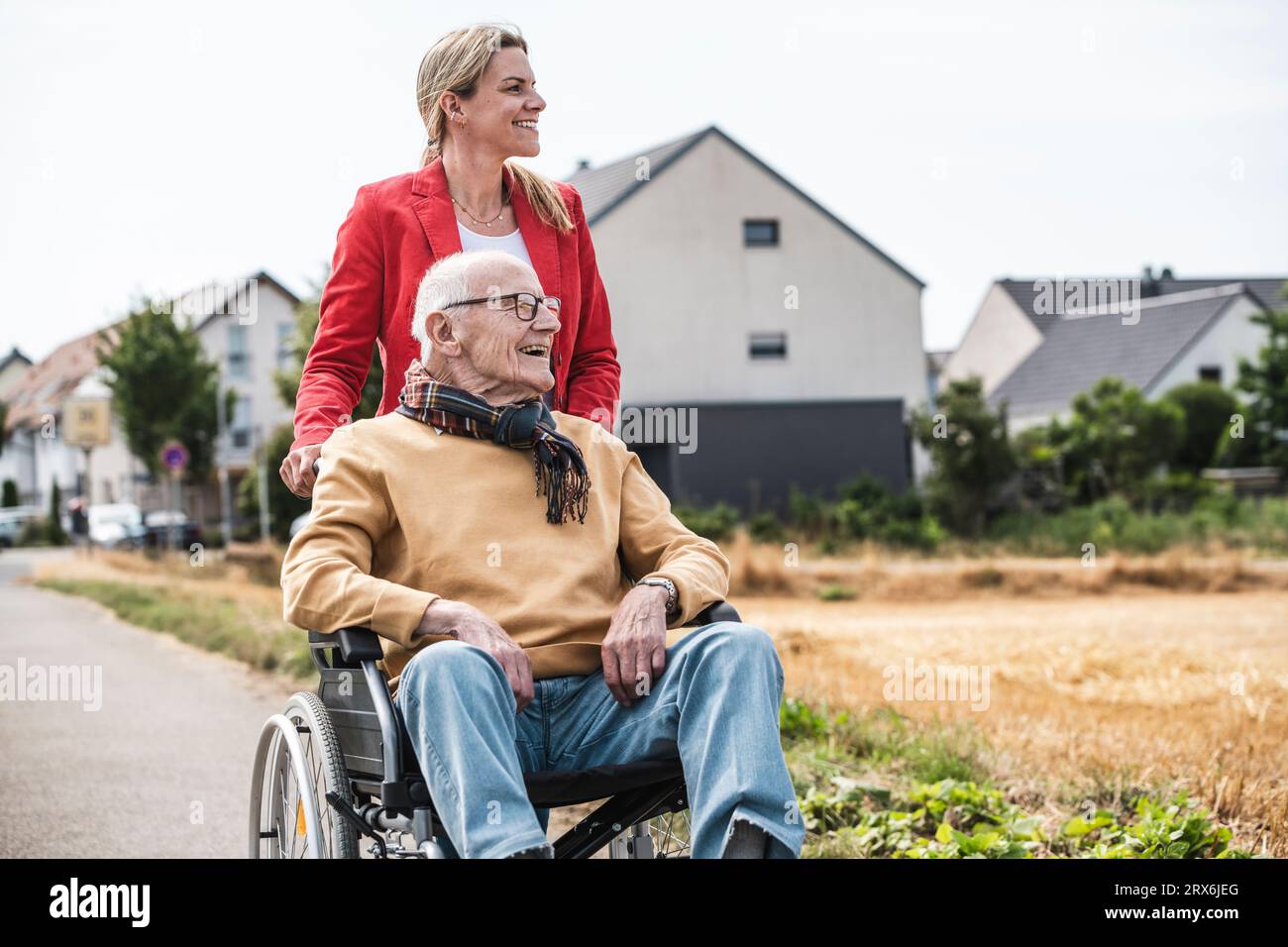 Donna felice con un uomo anziano seduto in sedia a rotelle su strada Foto Stock