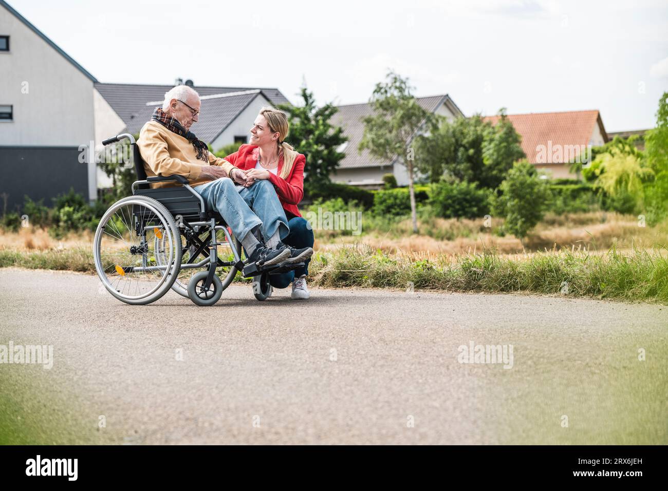 Donna che parla con un uomo anziano seduto in sedia a rotelle su strada Foto Stock