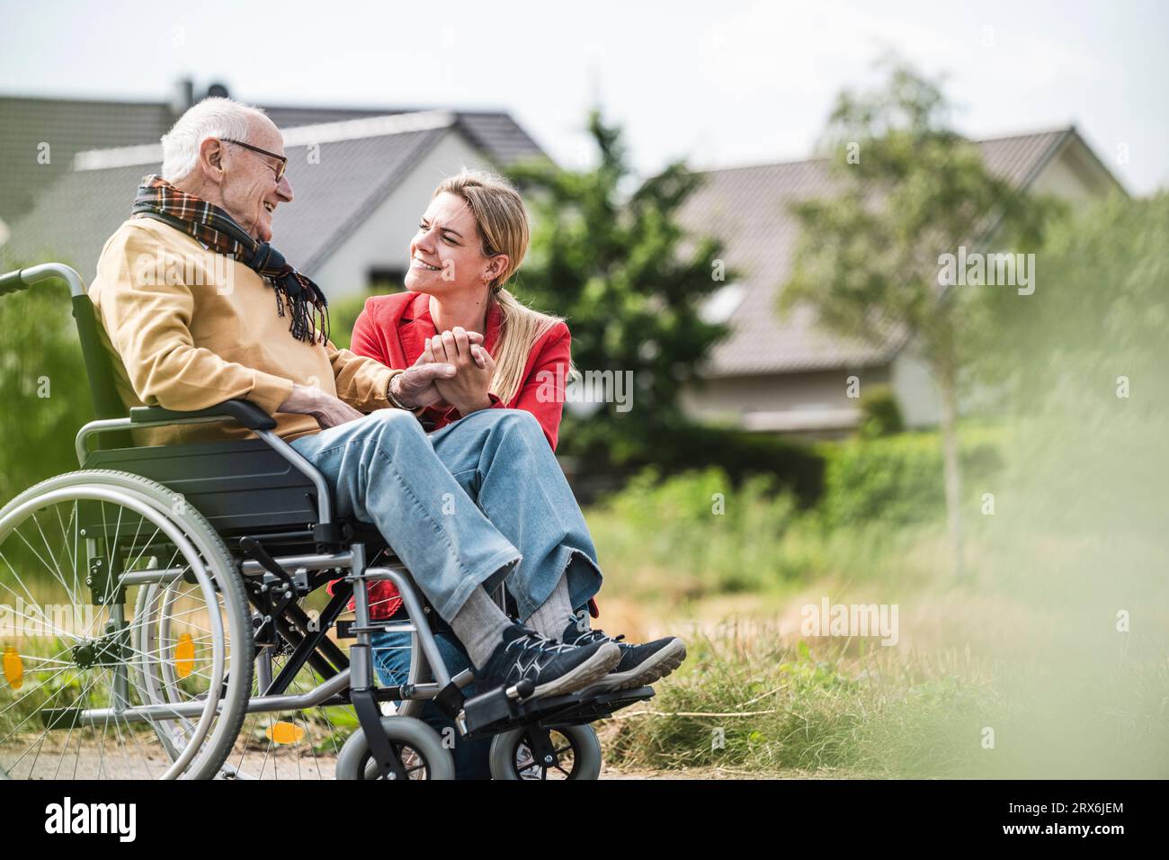 Donna sorridente che tiene per mano un uomo anziano seduto in sedia a rotelle Foto Stock