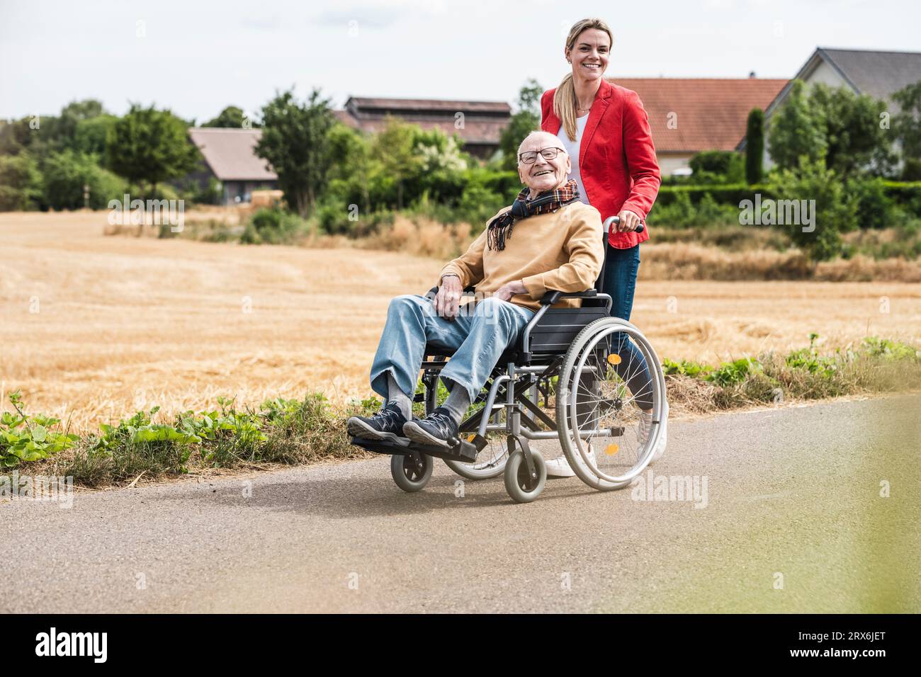 Donna sorridente che spinge un uomo anziano seduto in sedia a rotelle Foto Stock