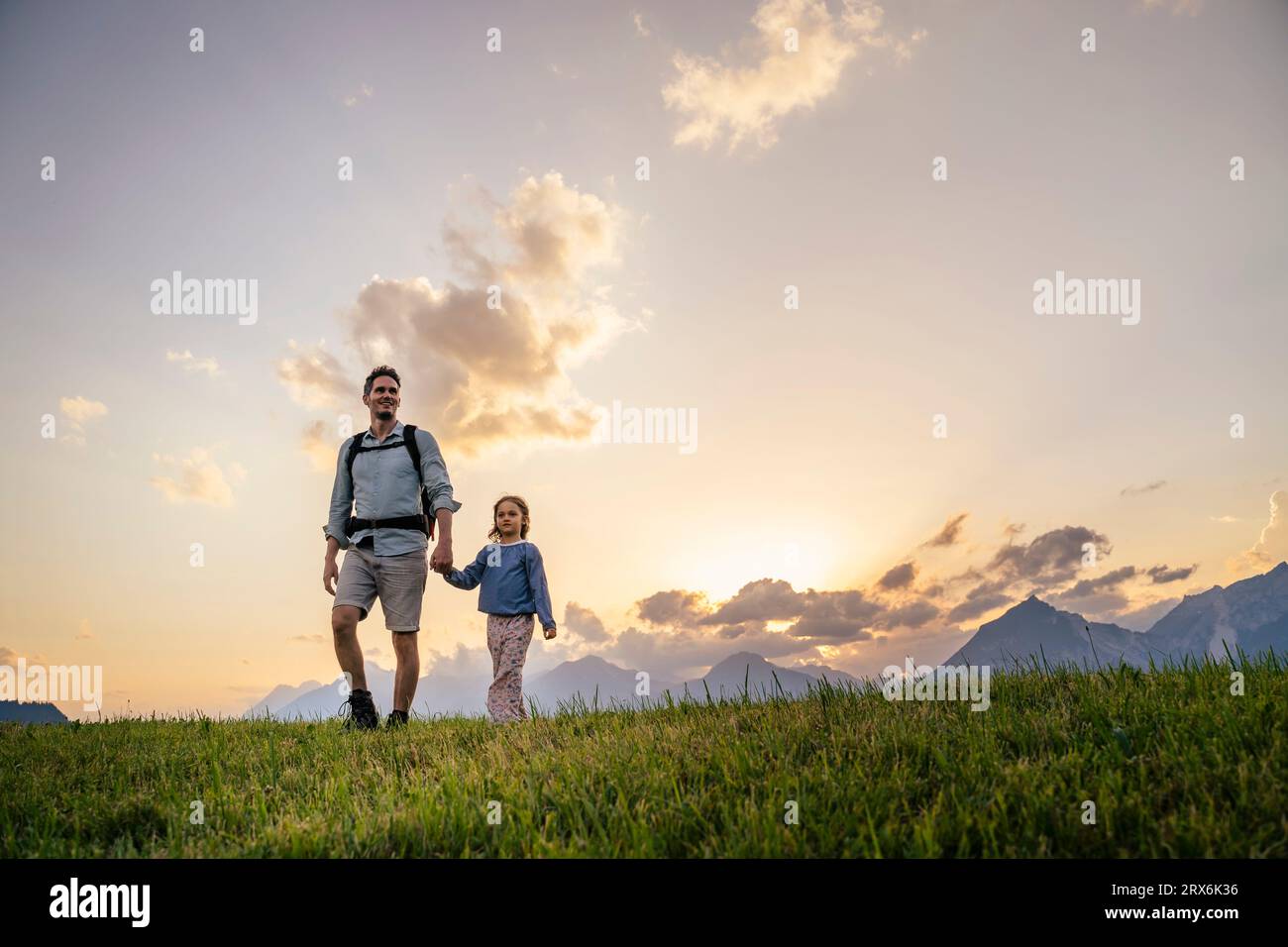 Figlia e padre che si tengono per mano e camminano sull'erba Foto Stock