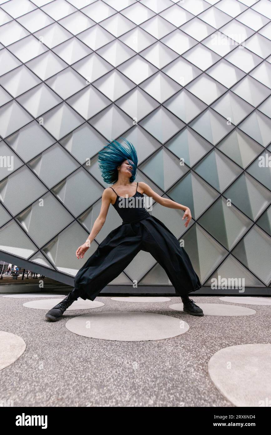 Ballerina con capelli blu tinti che balla vicino a un edificio moderno Foto Stock