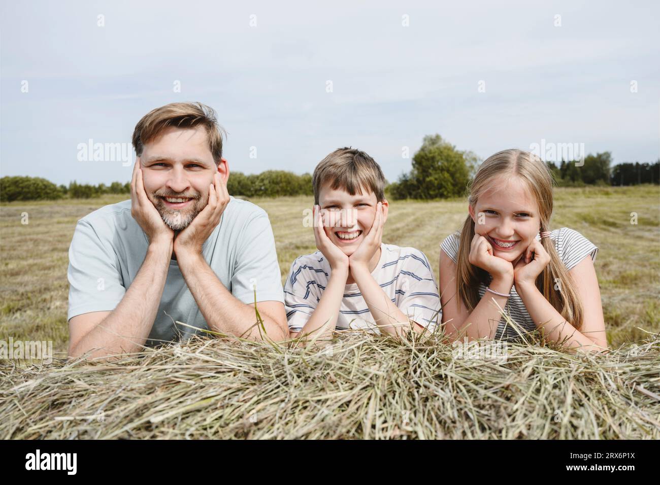 Padre sorridente e bambini con la mano sul mento appoggiata al fieno Foto Stock