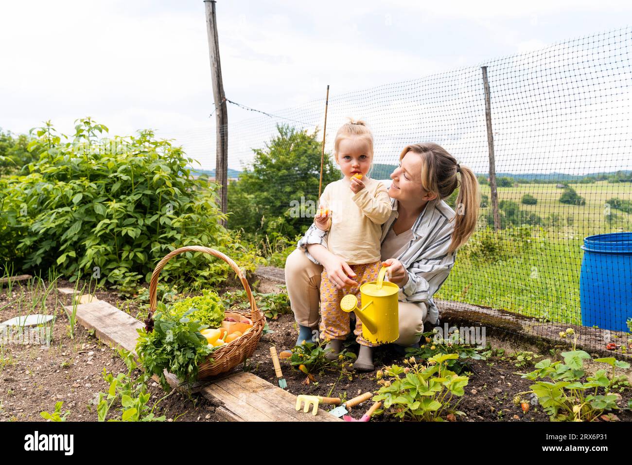 Madre sorridente con ragazza che mangia frutta in giardino Foto Stock