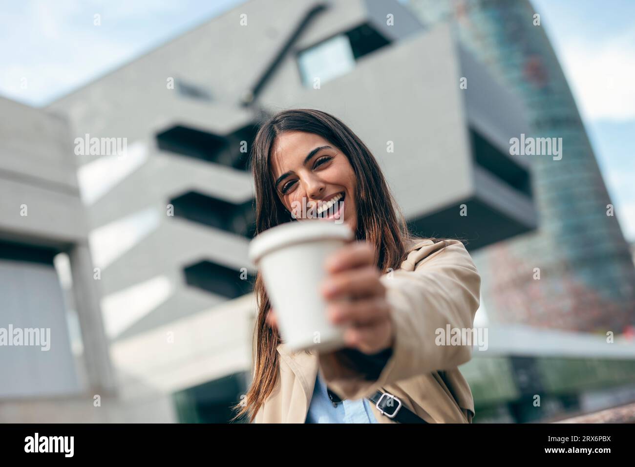 Giovane donna felice che tiene una tazza di caffè davanti all'edificio Foto Stock
