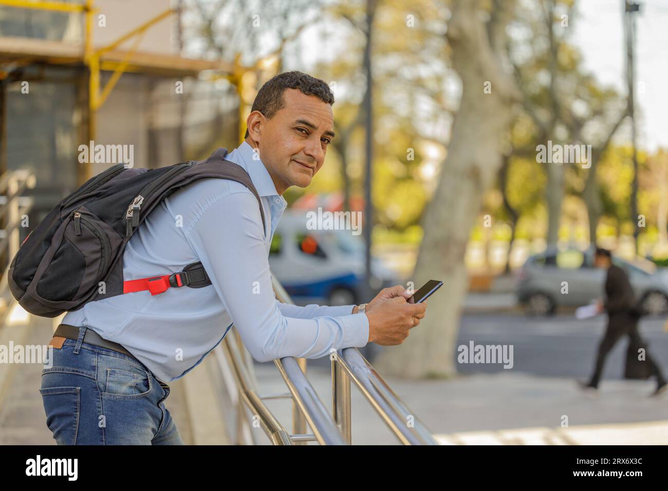 Uomo latino in camicia appoggiato su una ringhiera usando il suo cellulare con spazio per le copie. Foto Stock