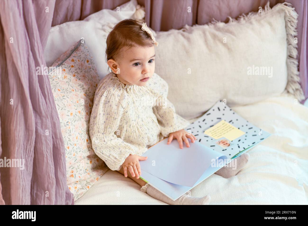 Carino, ragazza del bambino che siede sui cuscini che legge un libro Foto Stock