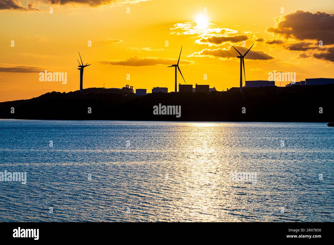 Il sole tramonta dietro le turbine eoliche nell'ex raffineria di petrolio Gulf a Waterston, Milford Haven nel Pembrokeshire, nel Galles occidentale, Regno Unito Foto Stock